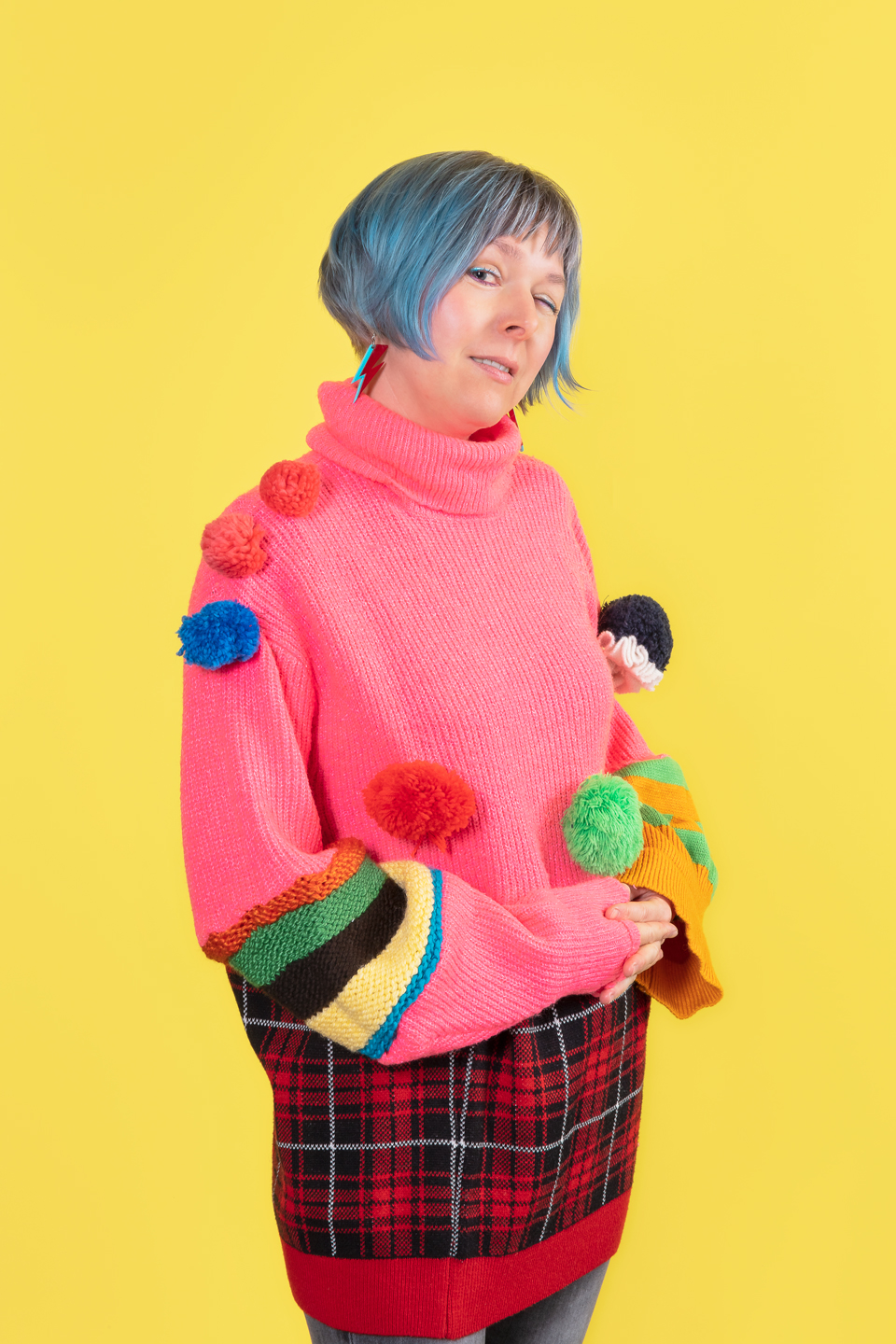 Une jeune femme au cheveux bleus, porte un pull bariolé en laine, beaucoup trop grand pour elle!